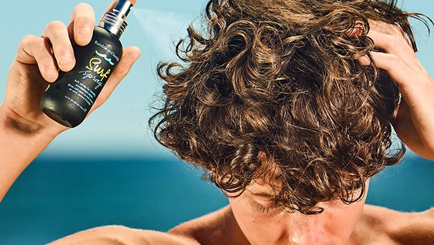 A close up of a man spraying hair product on his curly hair